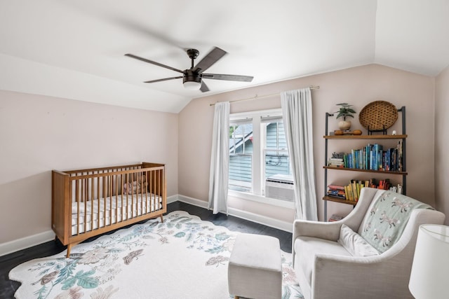 bedroom featuring lofted ceiling, wood finished floors, baseboards, a crib, and a ceiling fan