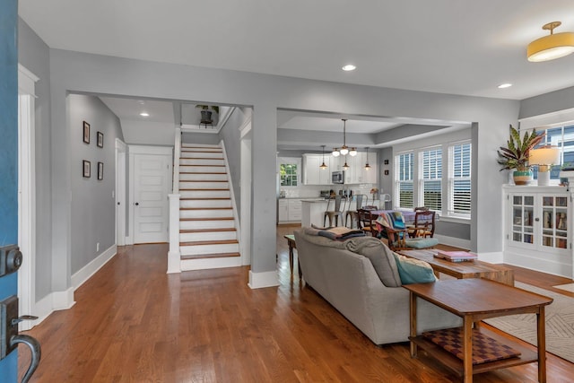 living room with stairs, baseboards, a chandelier, wood finished floors, and recessed lighting