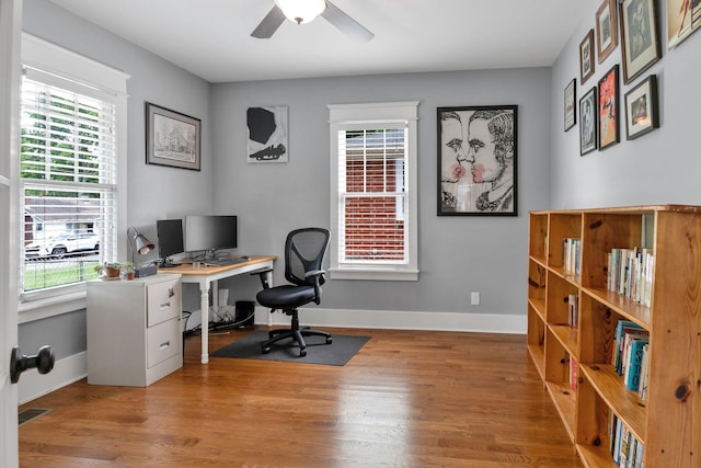 office space with healthy amount of natural light, ceiling fan, wood finished floors, and baseboards