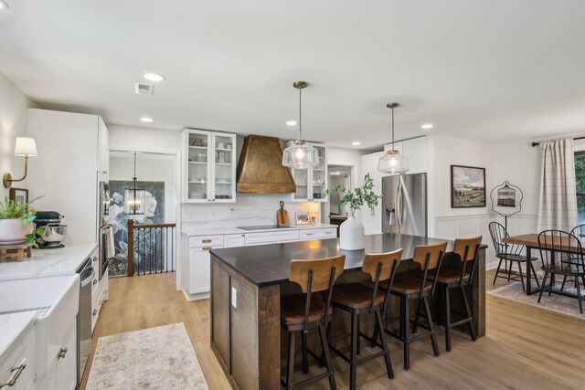 4151 Sadlersville Rd, Adams, TN 37010 - kitchen featuring appliances with stainless steel finishes, custom range hood, light wood-style floors, glass insert cabinets, and recessed lighting