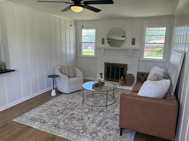 living room featuring wood finished floors, a ceiling fan, a fireplace, a decorative wall, and ornamental molding