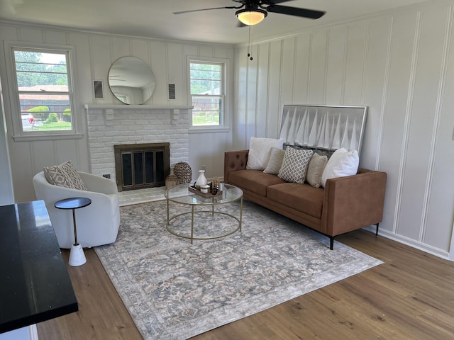 living area featuring a decorative wall, a ceiling fan, wood finished floors, crown molding, and a fireplace