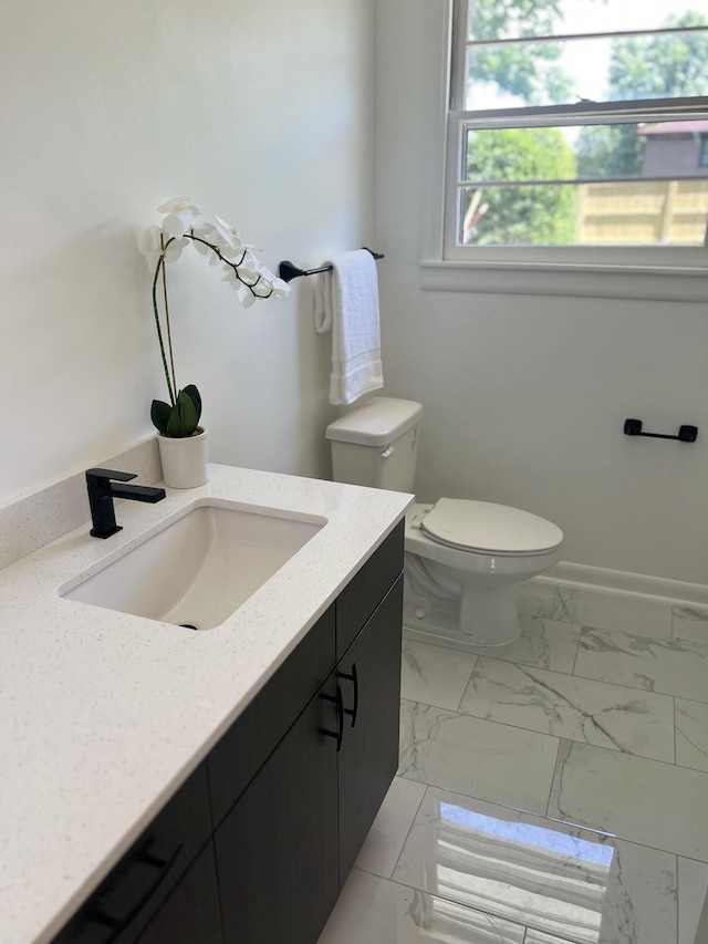half bath with vanity, toilet, and marble look tile flooring