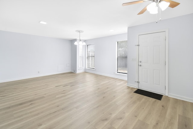 empty room featuring a chandelier, a ceiling fan, light wood finished floors, and baseboards