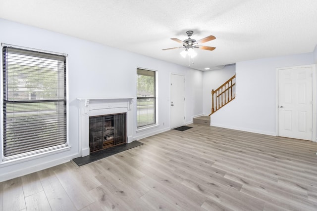 unfurnished living room featuring stairs, a ceiling fan, wood finished floors, a fireplace, and baseboards