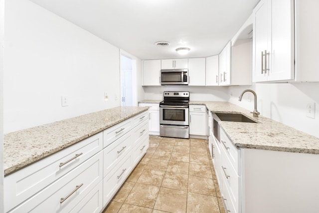 kitchen with stainless steel appliances, a sink, white cabinets, light stone counters, and light stone finish floors