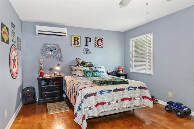 bedroom with an AC wall unit, wood finished floors, baseboards, and ceiling fan