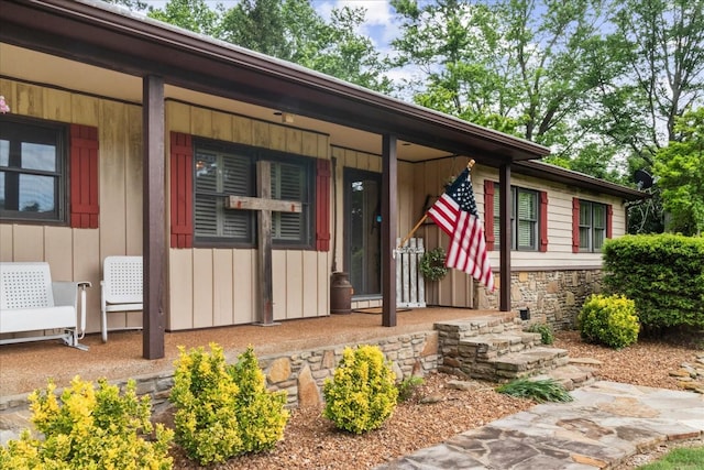 doorway to property with stone siding, board and batten siding, and a porch