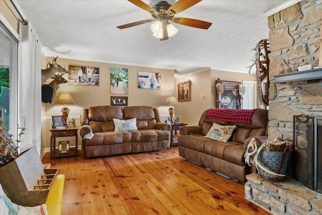 living area with a textured ceiling, a fireplace, light wood-type flooring, a ceiling fan, and ornamental molding
