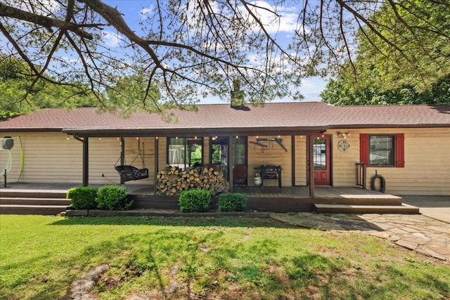rear view of house featuring a yard, a wooden deck, and roof with shingles