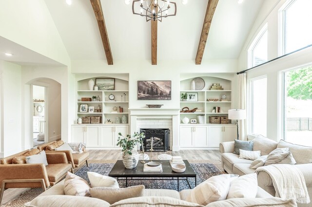 living room with arched walkways, light wood-style flooring, a chandelier, built in features, and beam ceiling