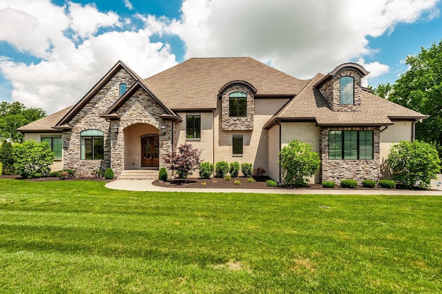 french country home with stone siding, a front yard, a shingled roof, and stucco siding