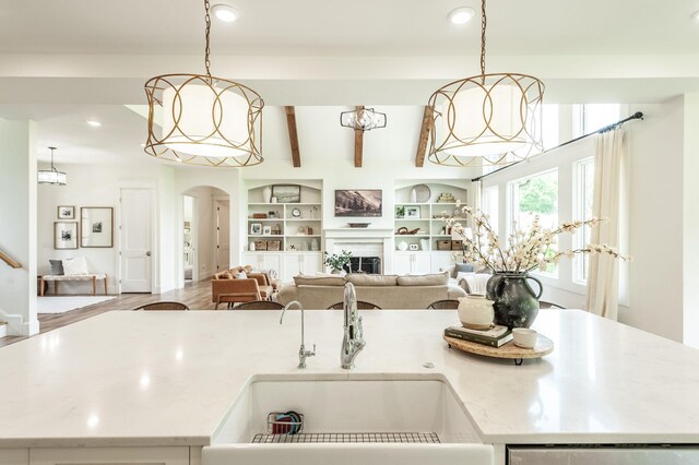 kitchen featuring a sink, arched walkways, recessed lighting, a fireplace, and hanging light fixtures