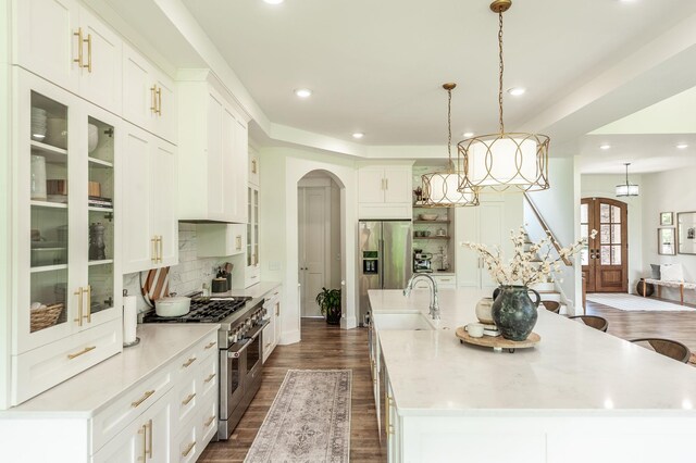 kitchen featuring high end appliances, a sink, arched walkways, recessed lighting, and a large island with sink
