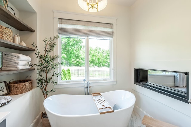full bath featuring healthy amount of natural light, a freestanding tub, baseboards, and marble look tile flooring