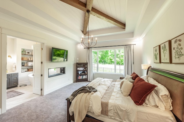 bedroom featuring a chandelier, light colored carpet, a glass covered fireplace, beam ceiling, and ensuite bath