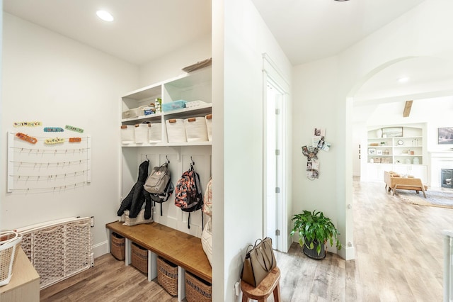 mudroom featuring light wood-type flooring, arched walkways, a glass covered fireplace, baseboards, and recessed lighting