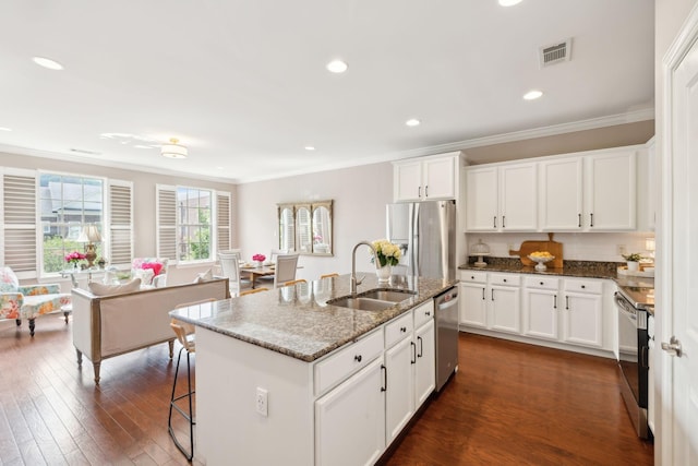 kitchen with a sink, stainless steel appliances, crown molding, dark stone counters, and a kitchen island with sink