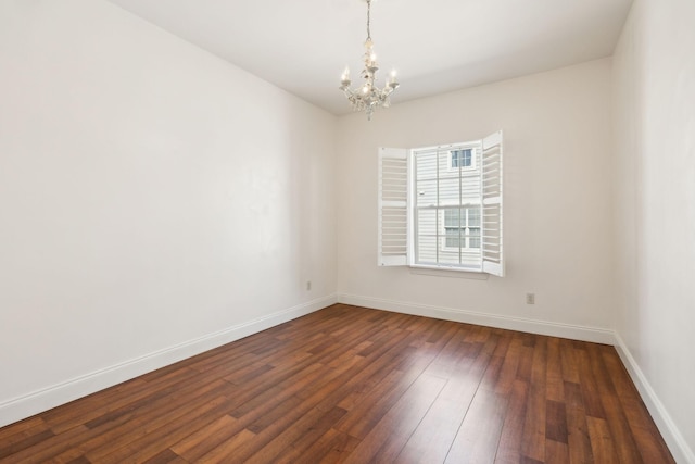 spare room with a chandelier, baseboards, and dark wood-style flooring
