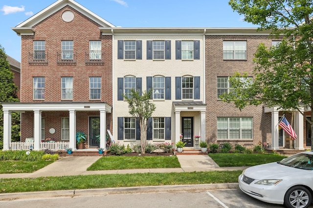 multi unit property with brick siding, uncovered parking, and a porch