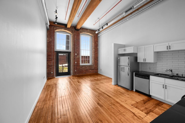 kitchen featuring stainless steel appliances, a sink, brick wall, baseboards, and dark countertops
