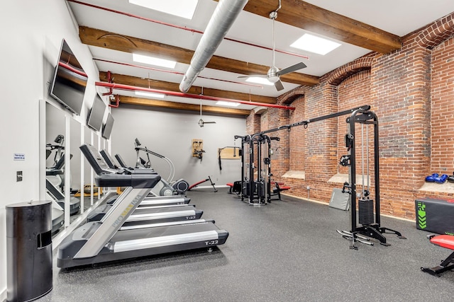 exercise room featuring brick wall, beam ceiling, and a ceiling fan