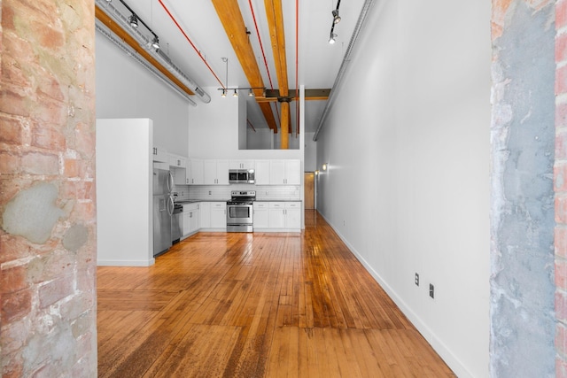 unfurnished living room featuring a towering ceiling, light wood-type flooring, and baseboards