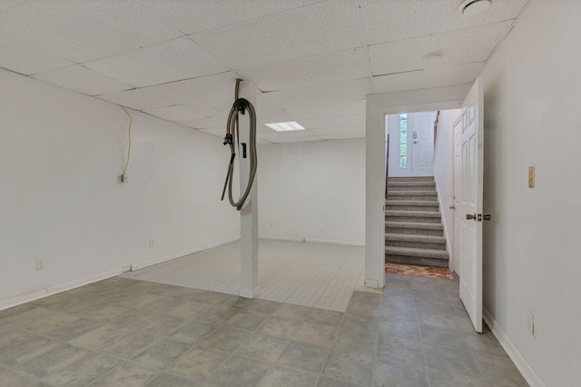 below grade area with a drop ceiling, stairway, and baseboards