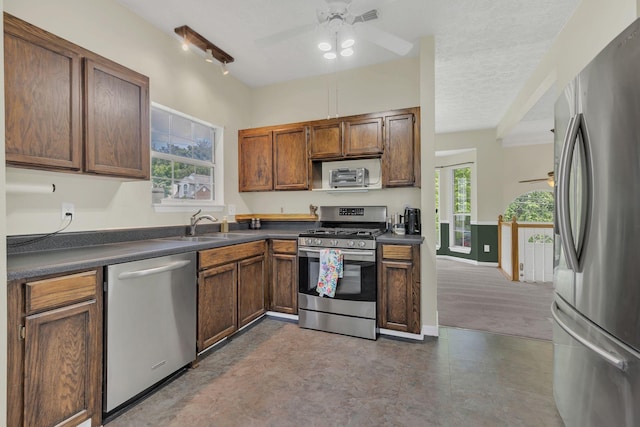 kitchen with appliances with stainless steel finishes, a ceiling fan, a sink, dark countertops, and a textured ceiling