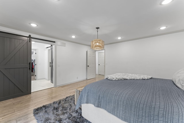 bedroom featuring light wood finished floors, a barn door, recessed lighting, crown molding, and baseboards