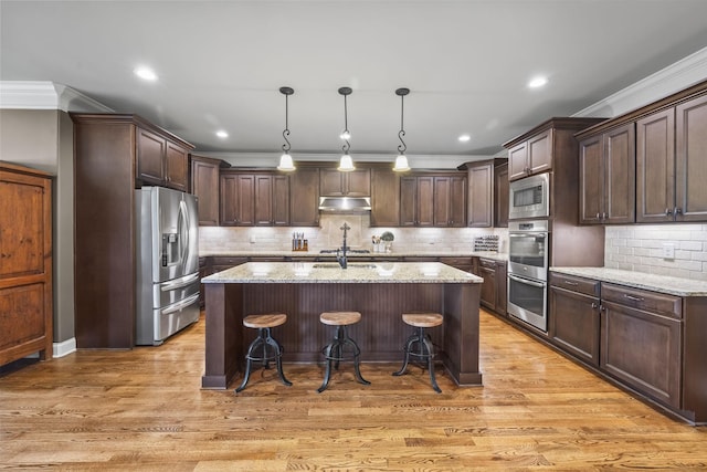 2979 Stewart Campbell Pt, Spring Hill, TN 37174 - kitchen with stainless steel appliances, under cabinet range hood, dark brown cabinets, decorative backsplash, and light stone countertops