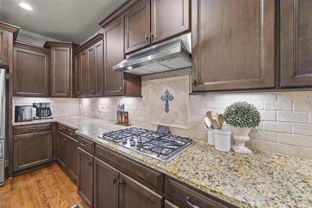 2979 Stewart Campbell Pt, Spring Hill, TN 37174 - kitchen with under cabinet range hood, light stone countertops, stainless steel gas stovetop, light wood-type flooring, and dark brown cabinets