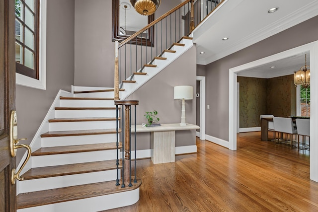 staircase with wood finished floors, baseboards, ornamental molding, a chandelier, and recessed lighting
