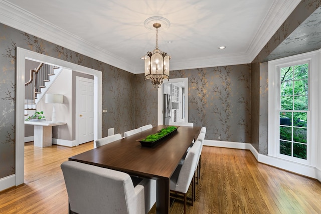 dining space with a chandelier, wood finished floors, baseboards, crown molding, and wallpapered walls