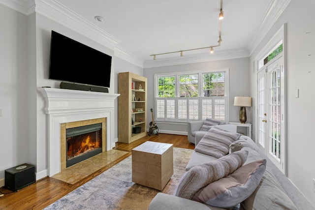 living room with wood finished floors, a tile fireplace, crown molding, track lighting, and baseboards