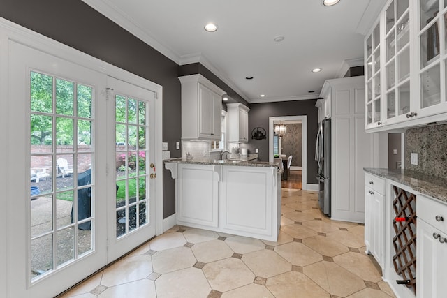 kitchen featuring freestanding refrigerator, backsplash, glass insert cabinets, ornamental molding, and light stone countertops