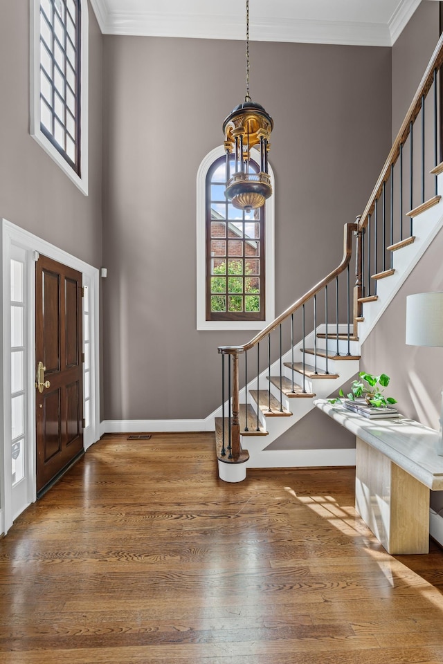 foyer featuring stairway, hardwood / wood-style flooring, crown molding, baseboards, and a high ceiling