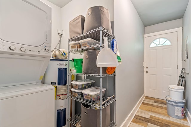 clothes washing area featuring stacked washer and clothes dryer, water heater, wood finished floors, and baseboards