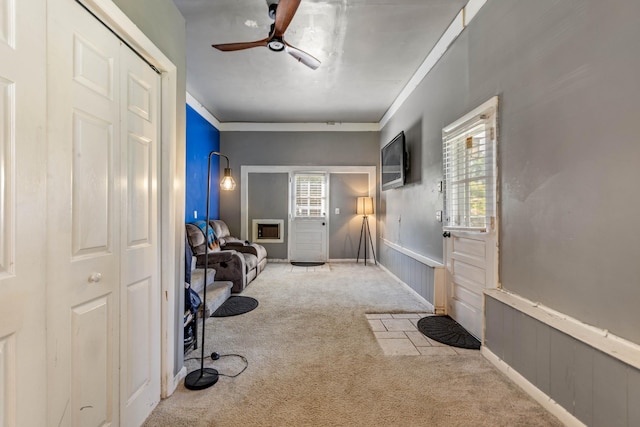 carpeted entryway with a ceiling fan, ornamental molding, and a wainscoted wall