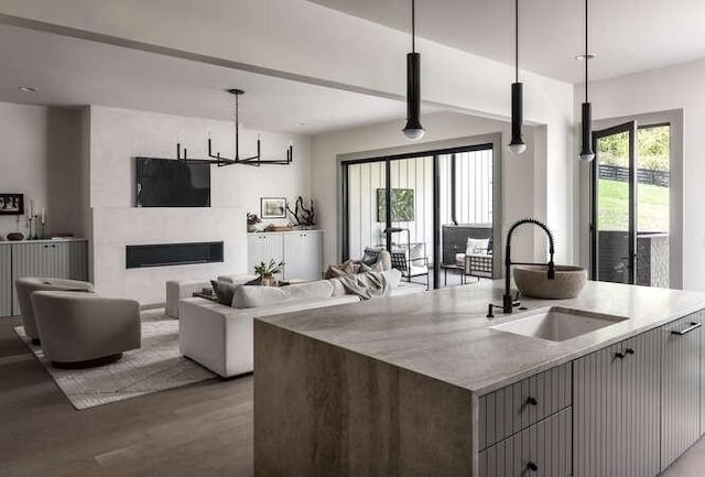 kitchen with a sink, wood finished floors, open floor plan, decorative light fixtures, and a center island with sink
