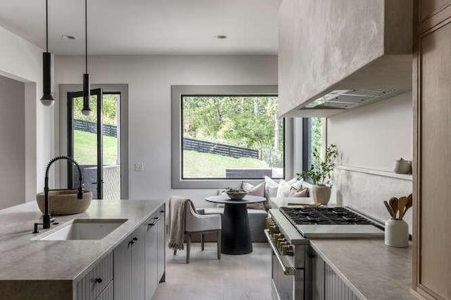 kitchen with a sink, stainless steel range, wall chimney exhaust hood, light countertops, and pendant lighting