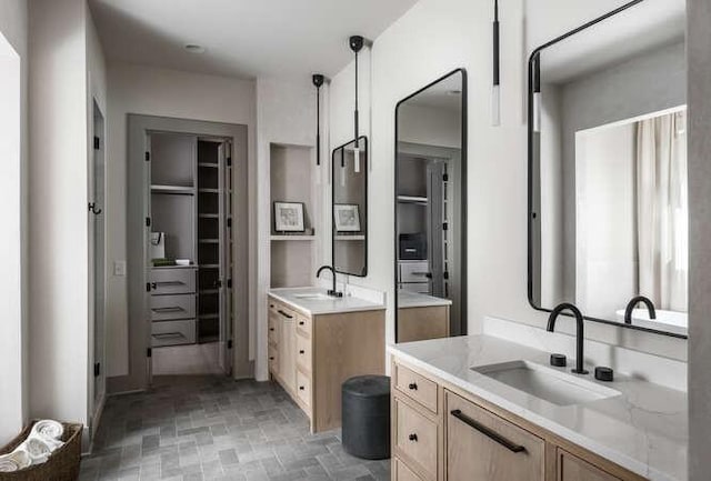 bathroom featuring brick patterned flooring, two vanities, and a walk in closet