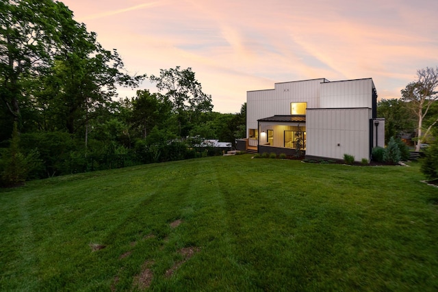back of house at dusk featuring a standing seam roof, a yard, and metal roof