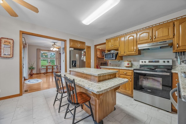 kitchen with stainless steel appliances, under cabinet range hood, a ceiling fan, and light marble finish floors