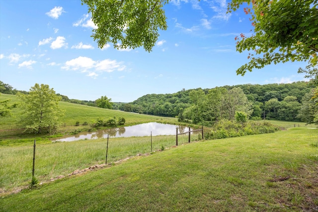 view of grassy yard featuring a water view and a wooded view
