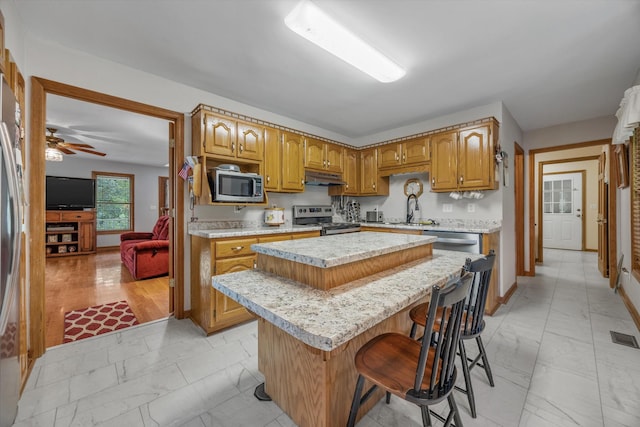 kitchen with light marble finish floors, appliances with stainless steel finishes, under cabinet range hood, and light countertops