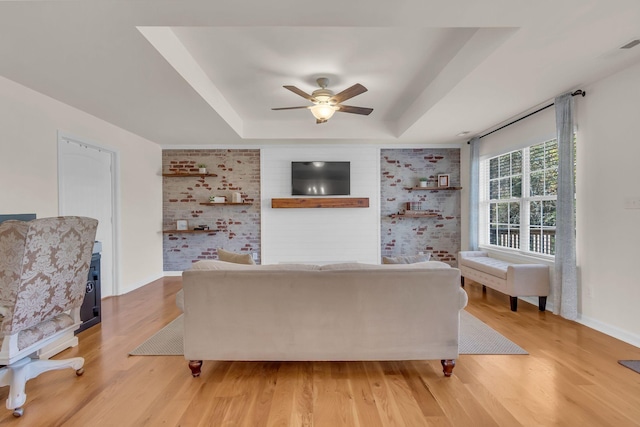 1032 Neeleys Bnd, Spring Hill, TN 37174 - living room featuring a raised ceiling, a ceiling fan, light wood-type flooring, baseboards, and brick wall