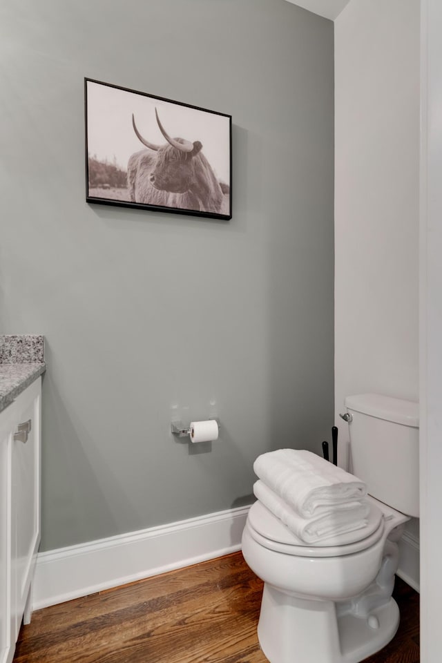 half bath with toilet, wood finished floors, baseboards, and vanity