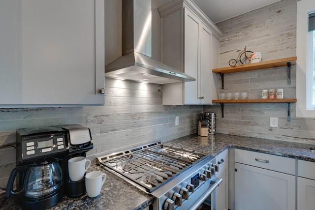 kitchen with high end stove, wall chimney exhaust hood, decorative backsplash, and open shelves