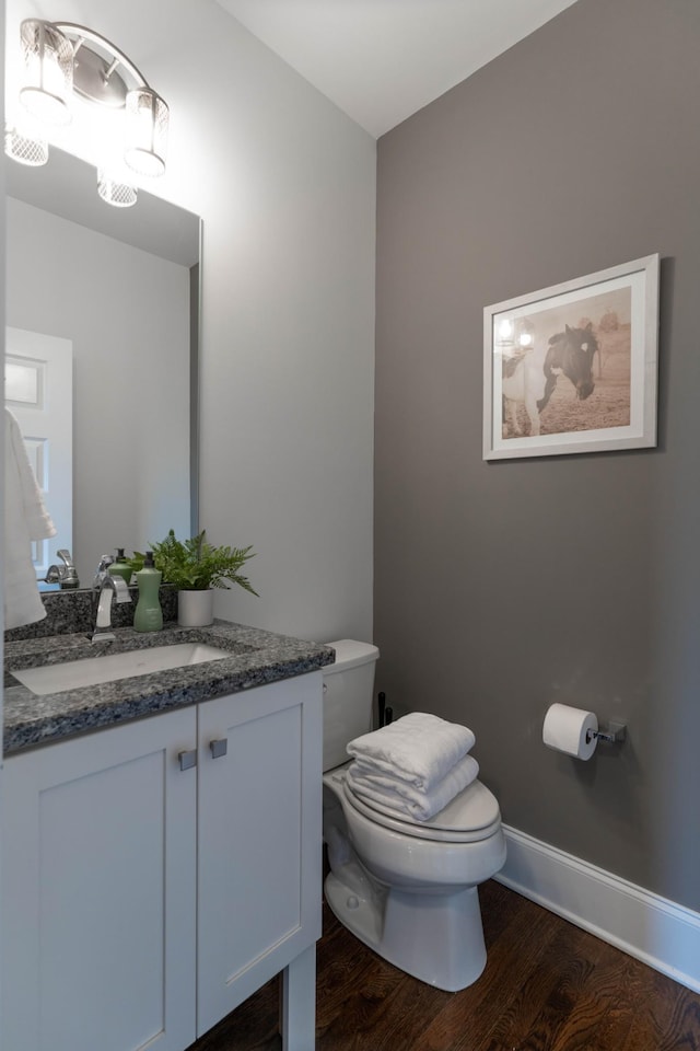 half bathroom featuring toilet, wood finished floors, vanity, and baseboards
